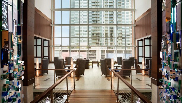 A hotel lobby with a modern design, featuring a spacious seating area, a staircase, and large windows offering views of the surrounding buildings. - Embassy Suites by Hilton Denver Downtown Convention Center (Denver)