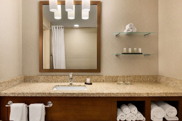 A bathroom with a granite countertop, a sink, a mirror, and shelves with towels and toiletries.