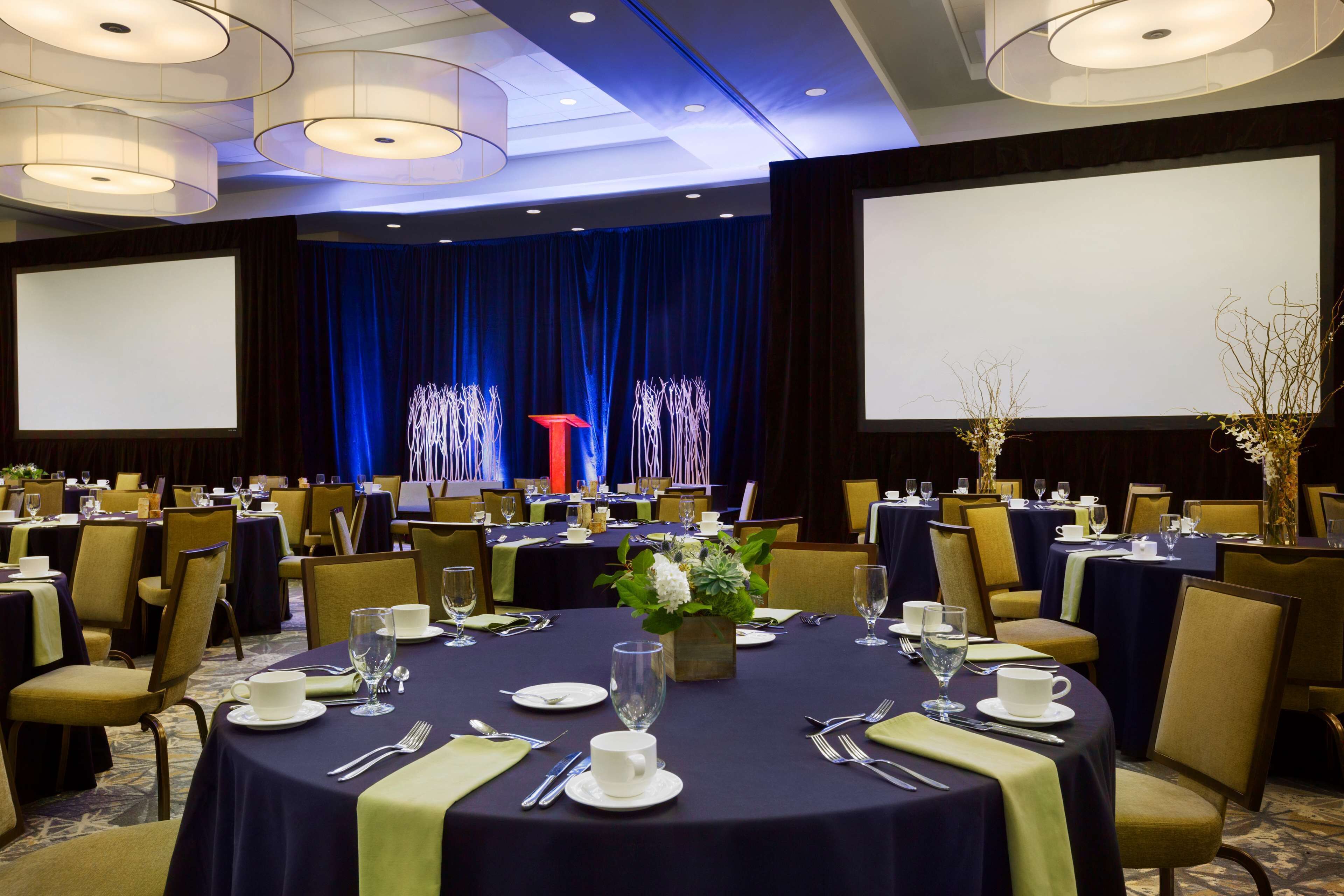 A conference room with round tables, chairs, and a stage with a podium.