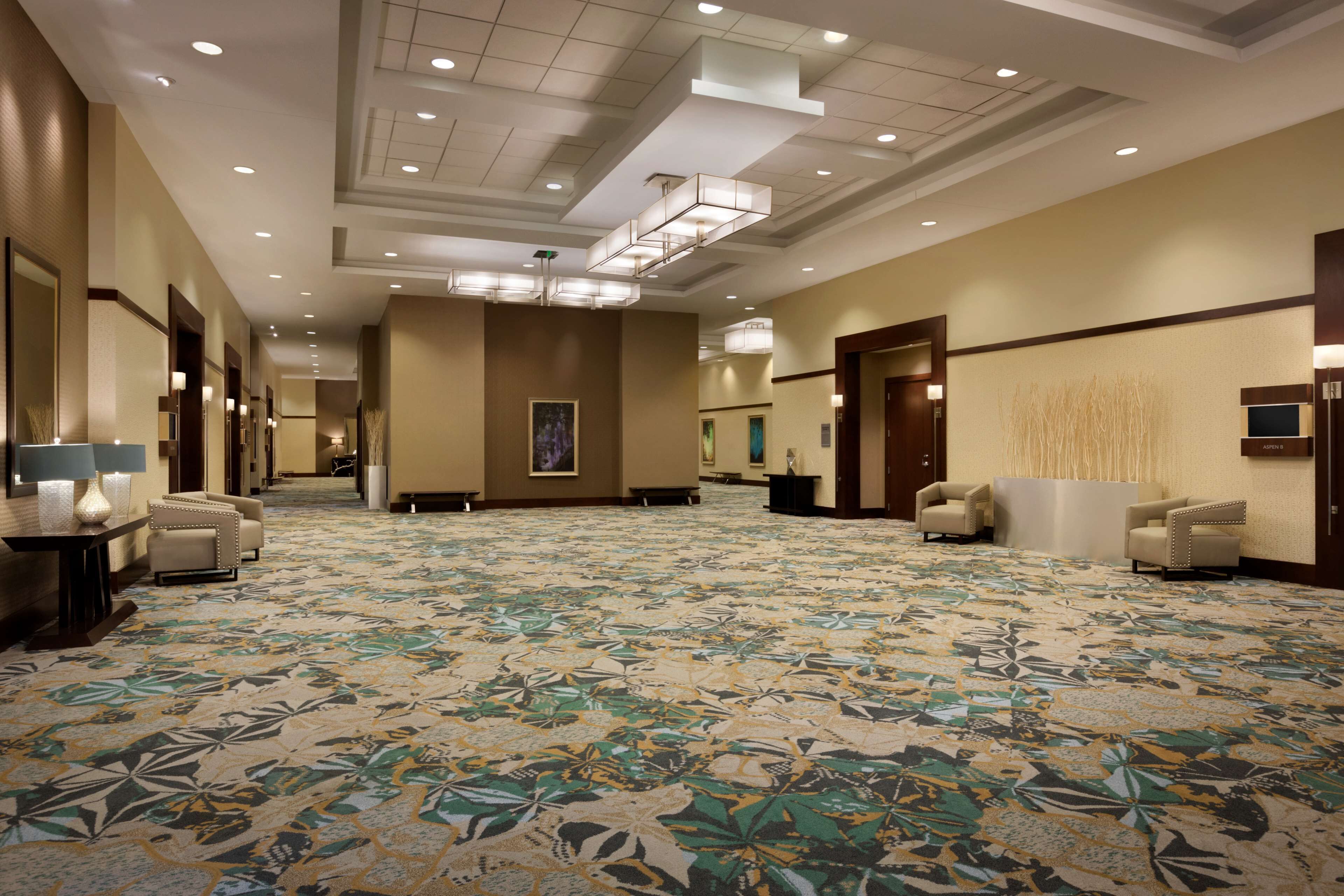 A spacious hotel lobby with a patterned carpet, multiple seating areas, and a modern ceiling design.