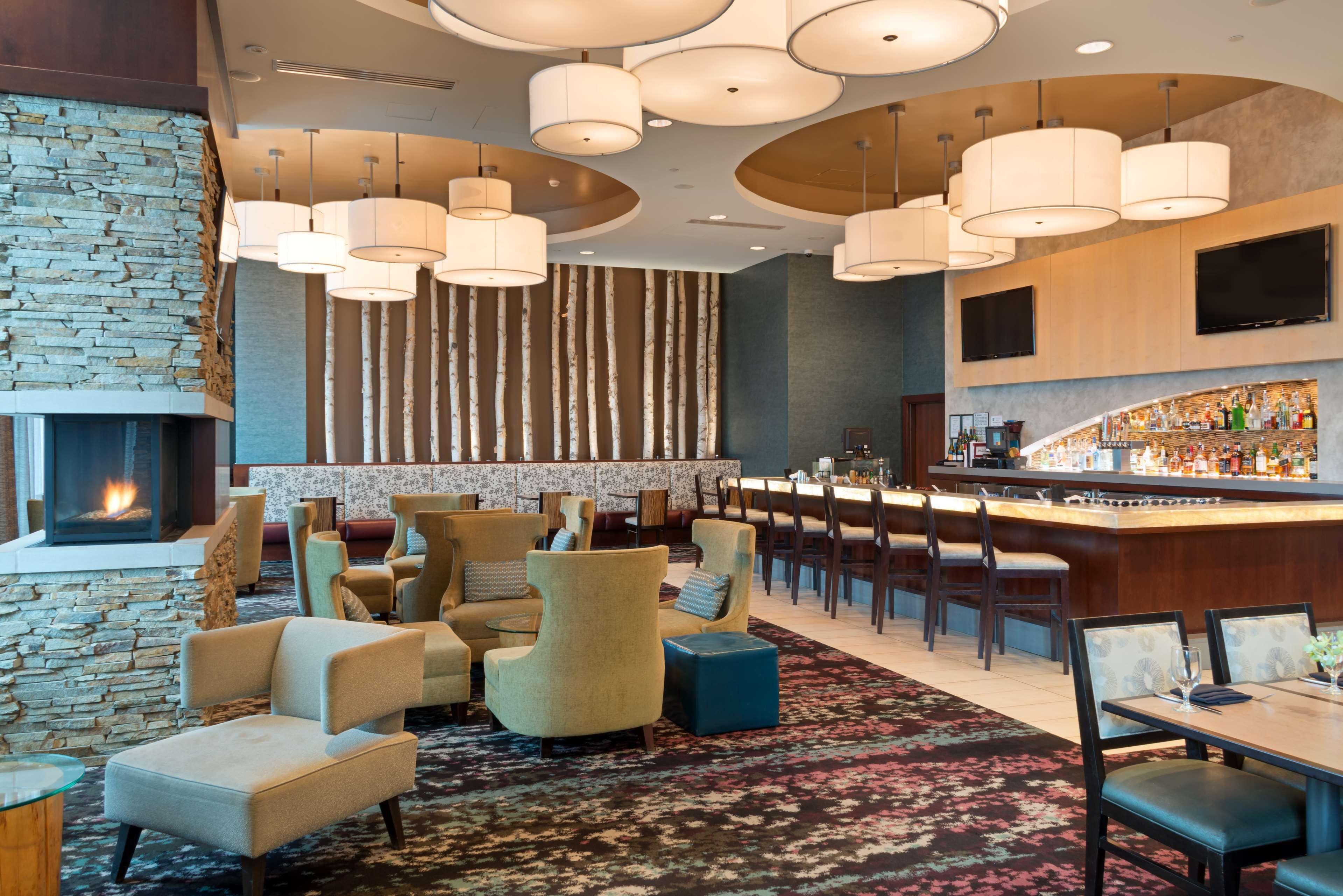 A hotel lobby with a stone fireplace, comfortable seating, a bar area, and a large TV screen.