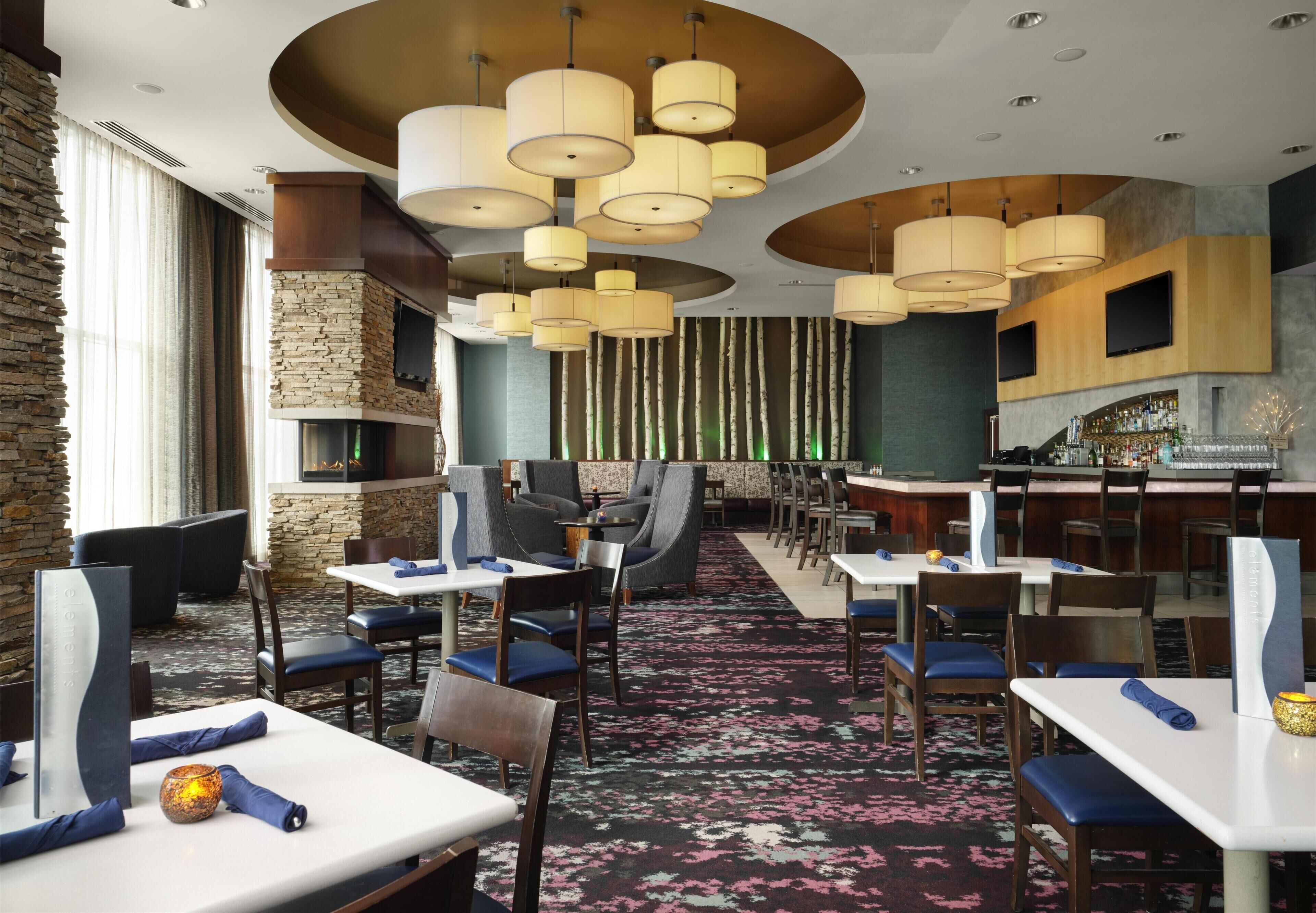 A restaurant with multiple tables and chairs, a bar area, and a stone wall.