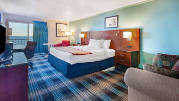 A hotel room with a bed, a desk, a chair, a small table, and a view of the sea through a window.
