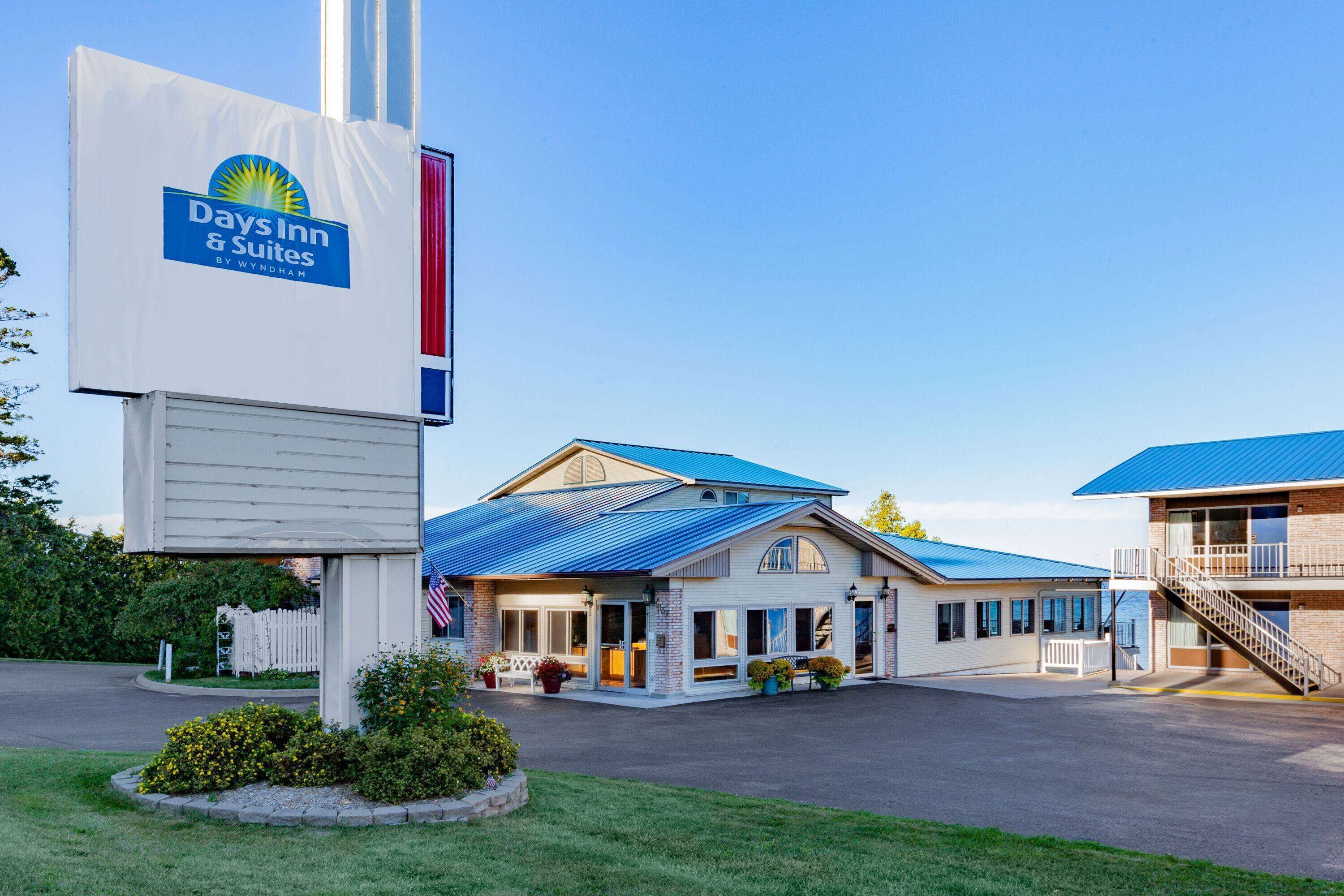 A Days Inn & Suites by Wyndham with a blue roof, a white facade, and a flagpole with the hotel’s logo.