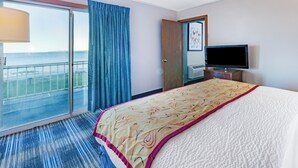 A hotel room with a large bed, a television, a sliding glass door to a balcony, and a view of the sea.