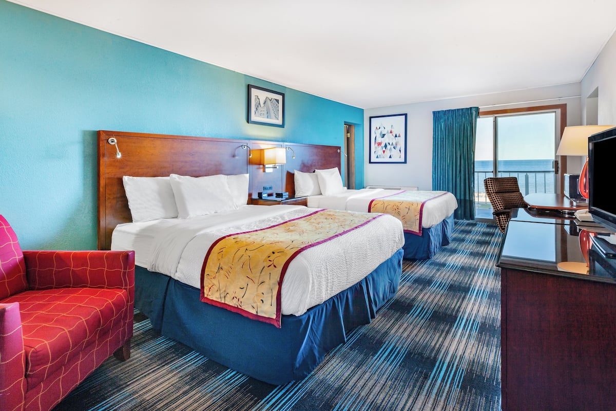 A hotel room with two beds, a desk, a chair, and a view of the ocean.