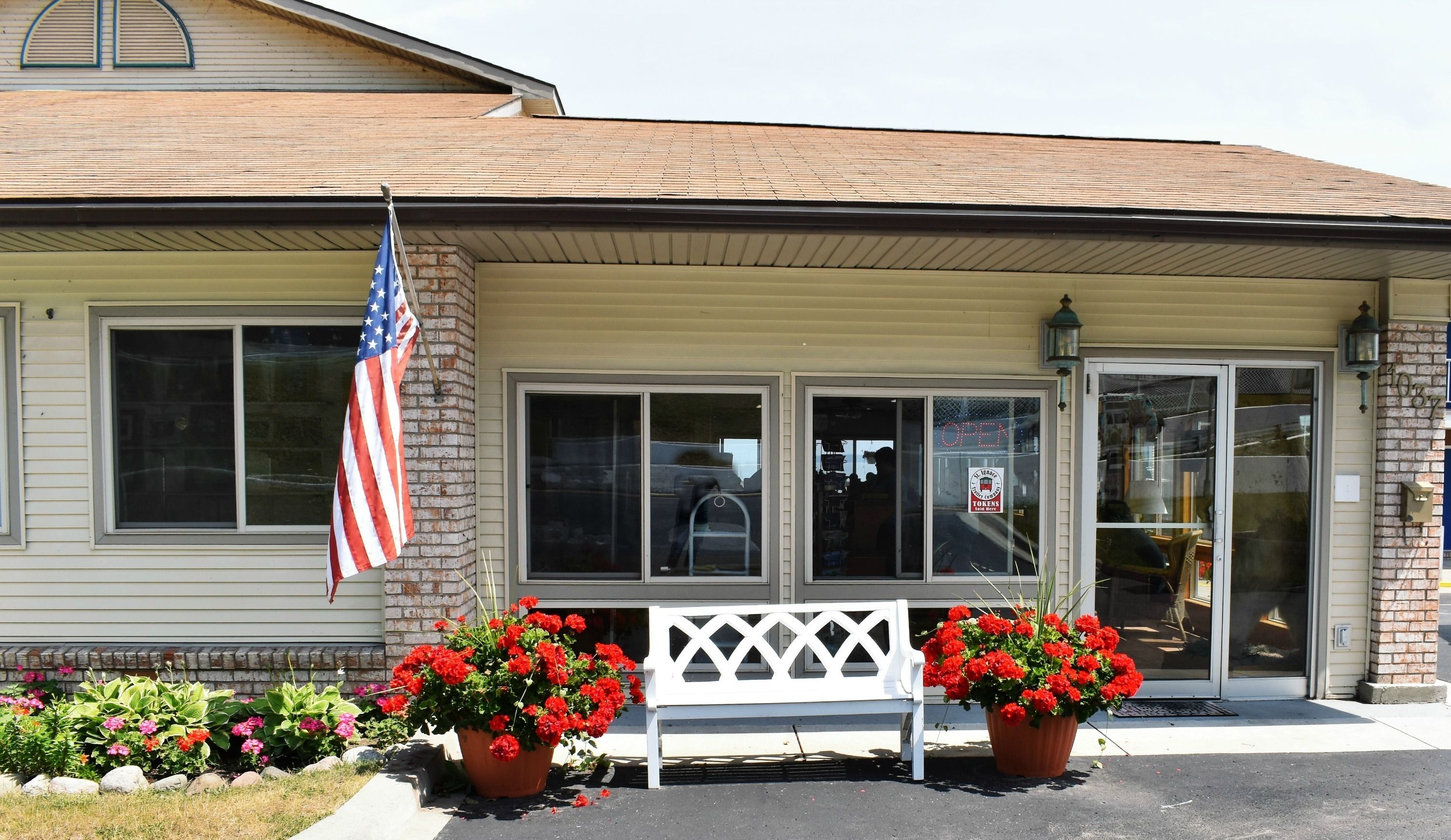A building with a brick facade, large windows, and a white porch with a bench.