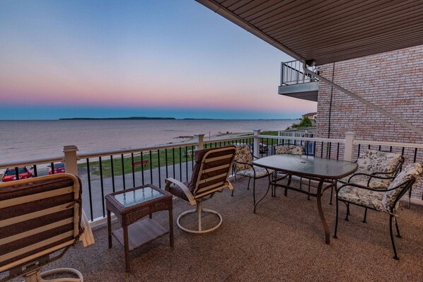 A balcony with a view of the sea, furnished with wicker chairs and a table.