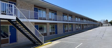 Un motel de dos pisos, un estacionamiento y un cielo azul despejado.