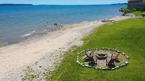 Une plage avec un foyer et des chaises disposées en cercle, offrant une vue sur une mer calme.