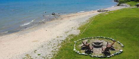 A beach with a fire pit and chairs arranged in a circle, overlooking a calm sea.