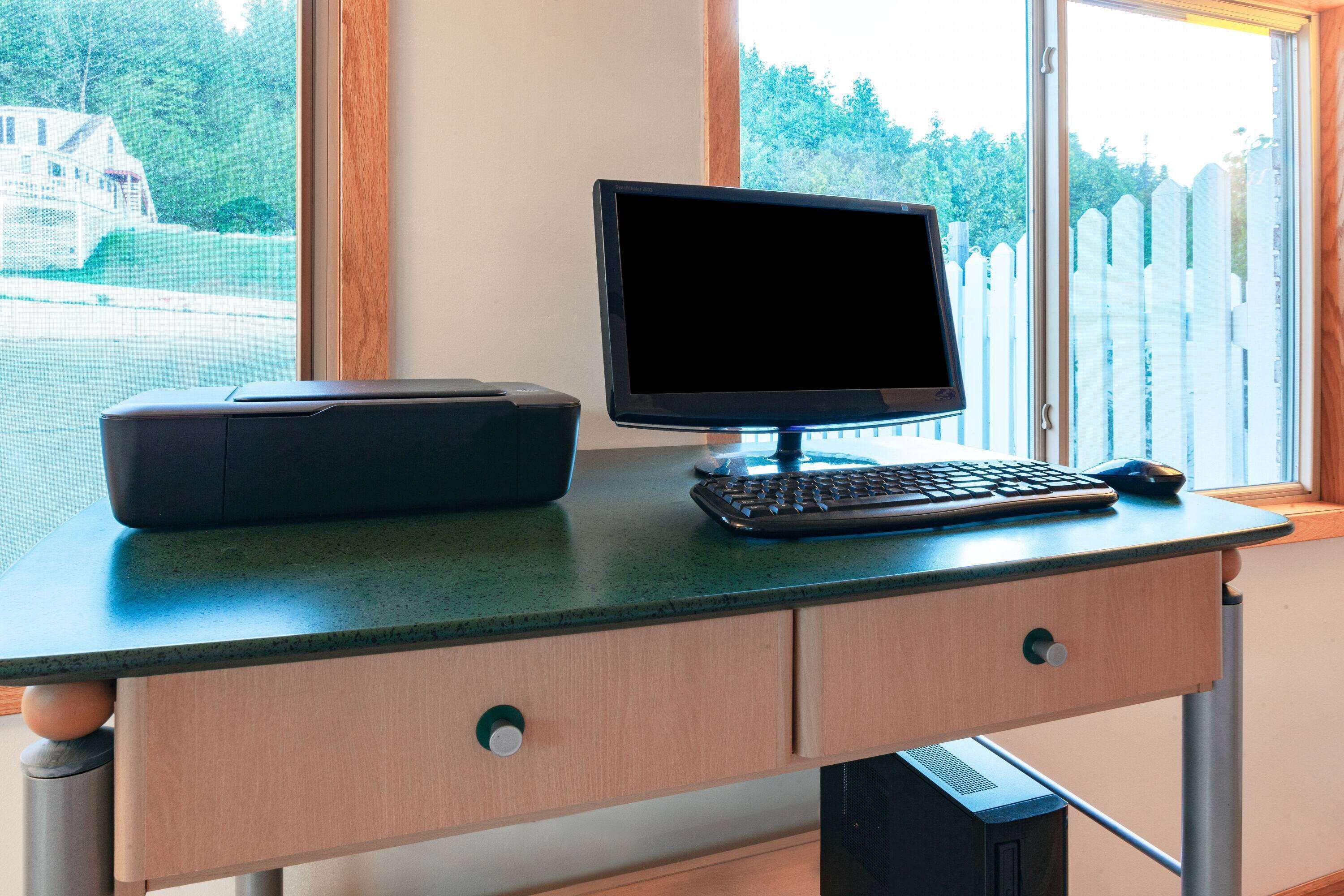 A workspace with a computer monitor, keyboard, and printer on a desk by a window.