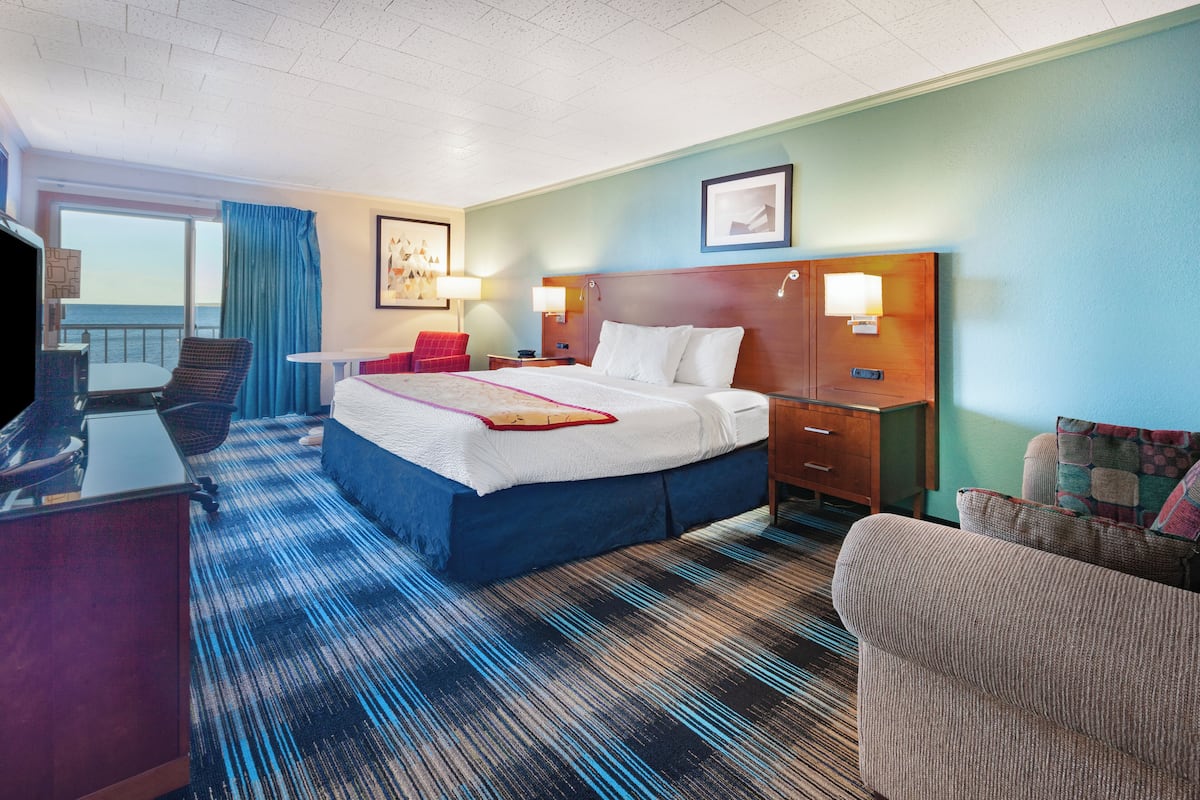 A hotel room with a large bed, a desk, a chair, and a view of the sea.