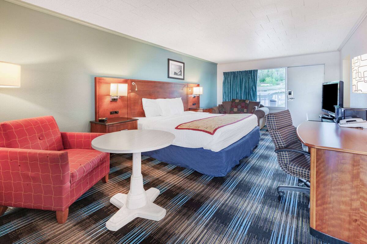 A hotel room with a bed, a desk, a chair, a table, and a TV.
