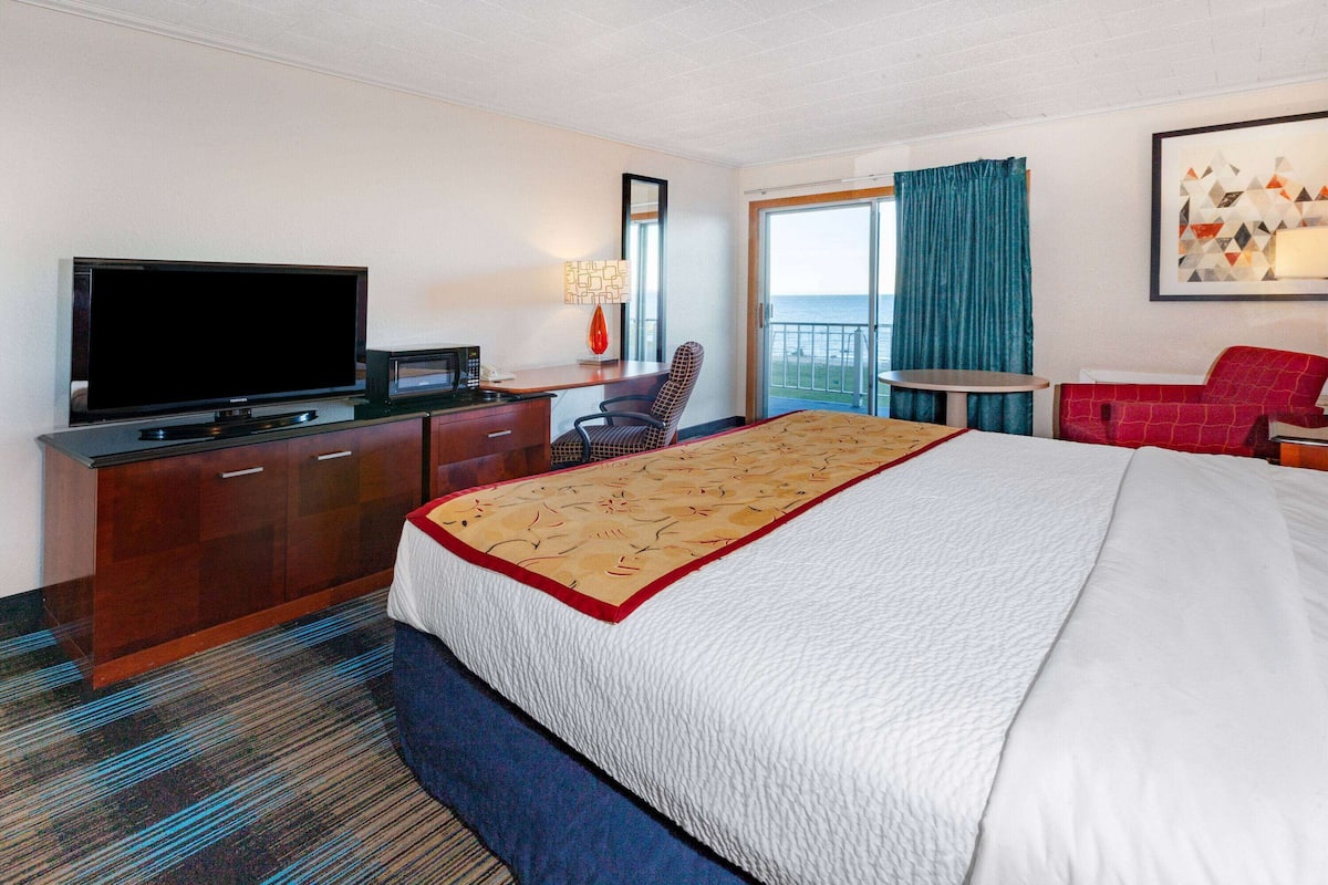 A hotel room with a large bed, a television, a desk with a computer, a chair, and a balcony with a view.