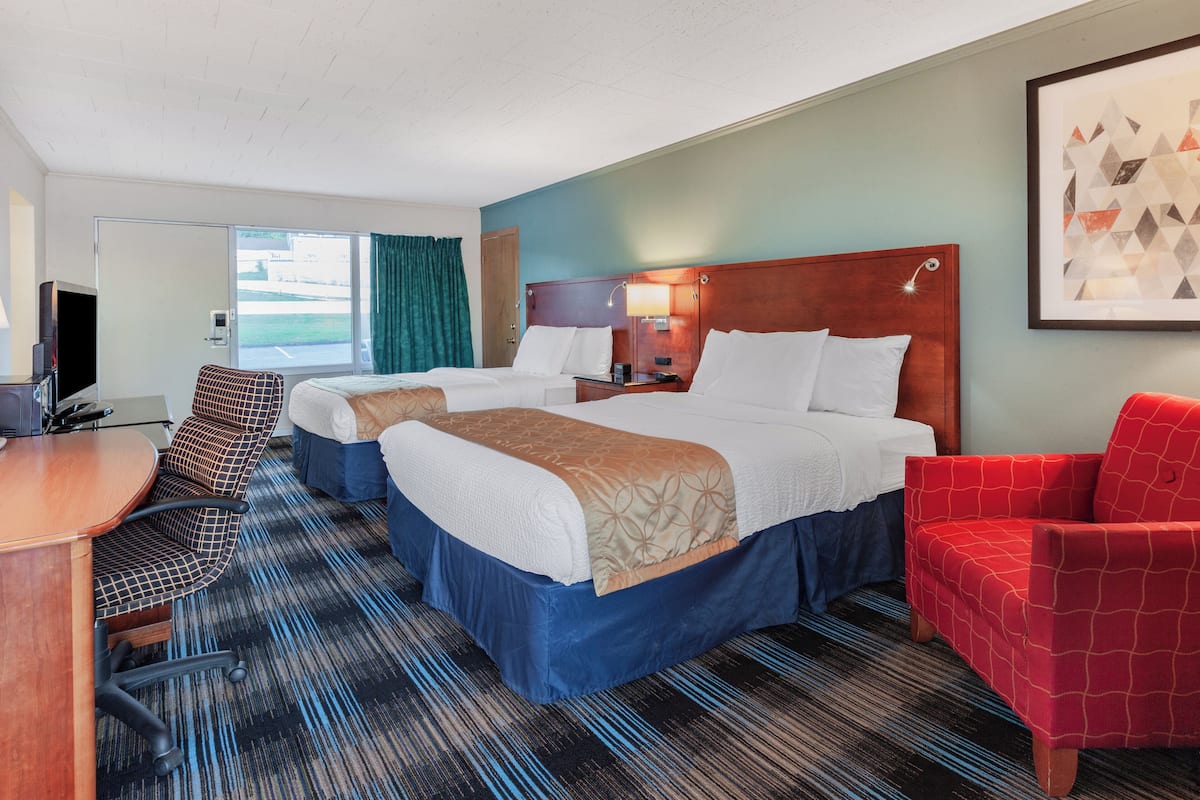 A hotel room with two beds, a desk, a chair, and a TV.