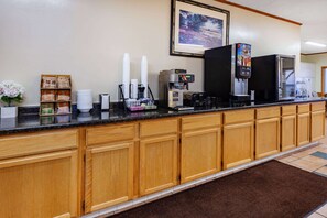 A hotel reception area with a long counter, wooden cabinets, a coffee machine, a beverage dispenser, and a framed picture on the wall.
