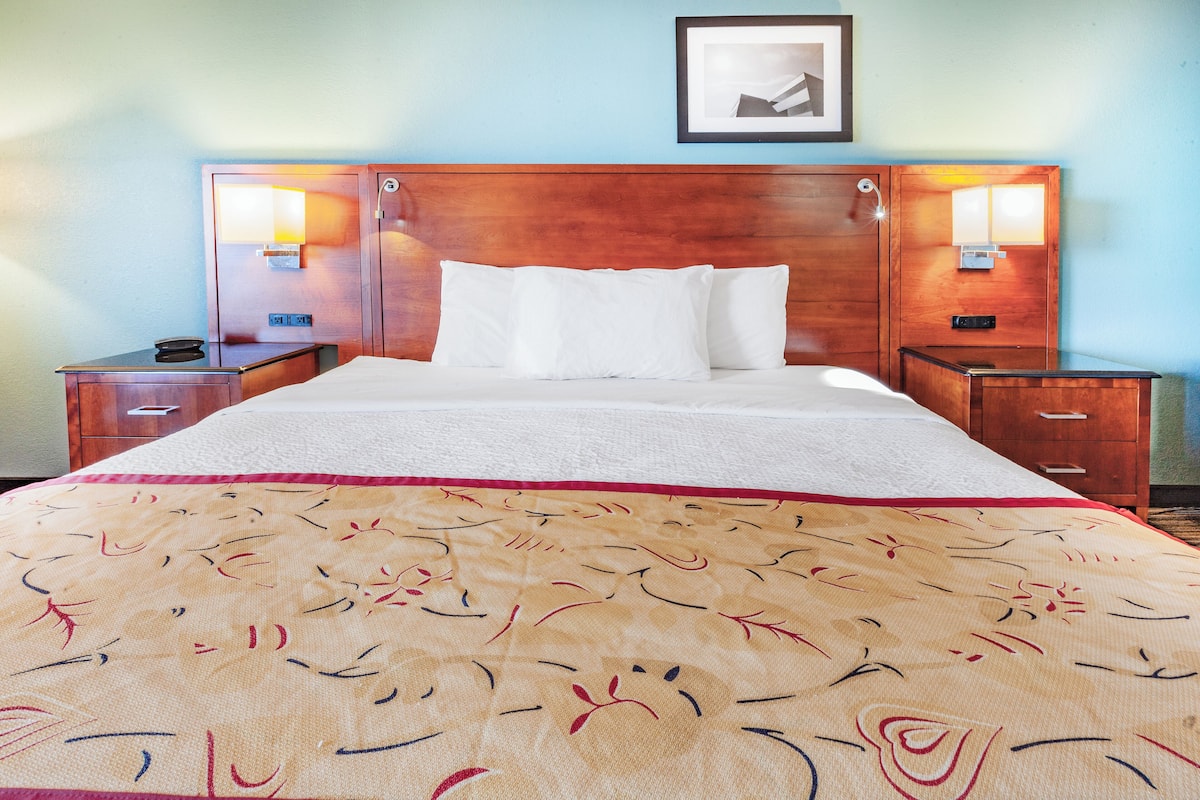 A hotel room with a large bed, two bedside tables, a wooden headboard, and two wall-mounted lamps.