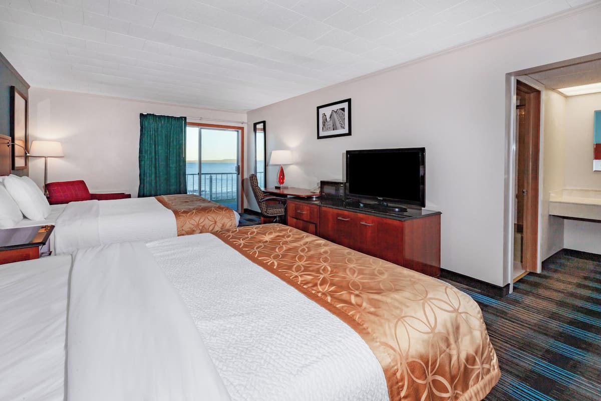 A hotel room with two beds, a desk with a television, a chair, and a view of the sea.