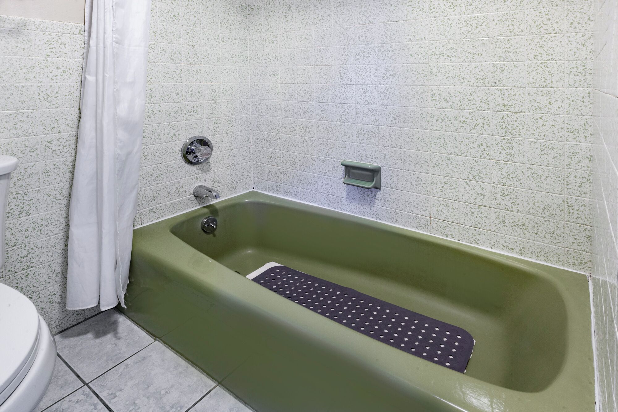 Ein Badezimmer mit einer grünen Badewanne, weiß gefliesten Wänden, einer weißen Toilette und einer Duschvorhang.