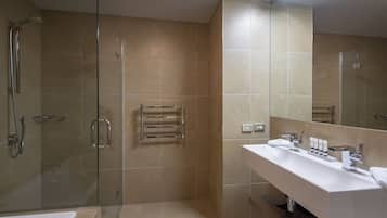 A modern bathroom with a glass-enclosed shower, a white sink with toiletries, and a large mirror.