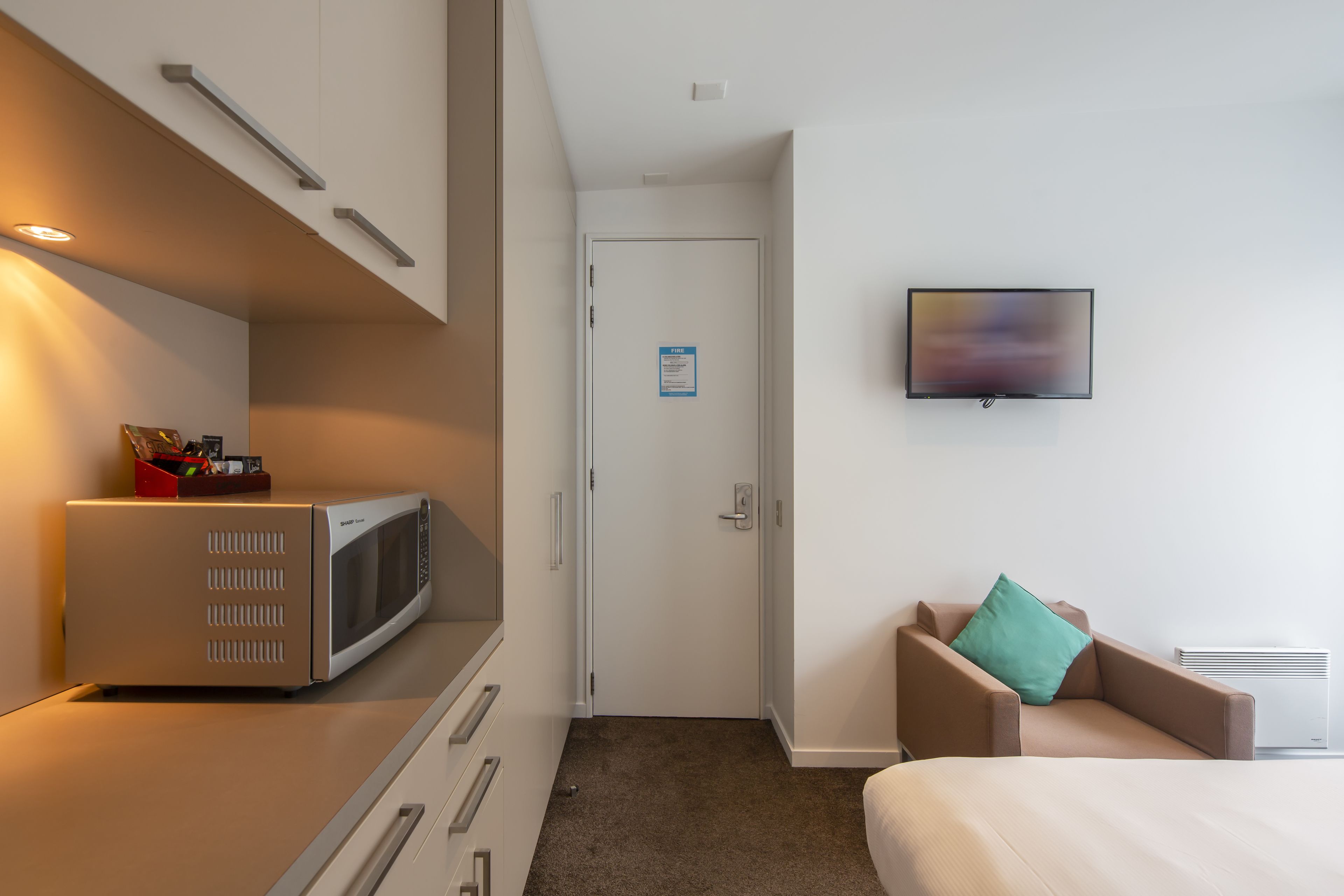 Habitación de hotel con microondas, televisión, cama, silla y puerta con un letrero.