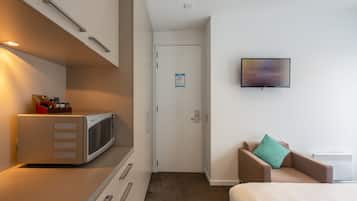 Habitación de hotel con microondas, televisión, cama, silla y puerta con un letrero.