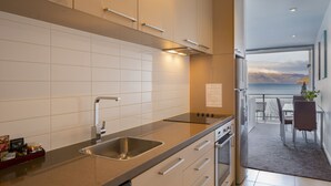 Eine moderne Küche mit Spüle aus Edelstahl, weißen Schränken und Blick auf einen Balkon mit schöner Landschaft.