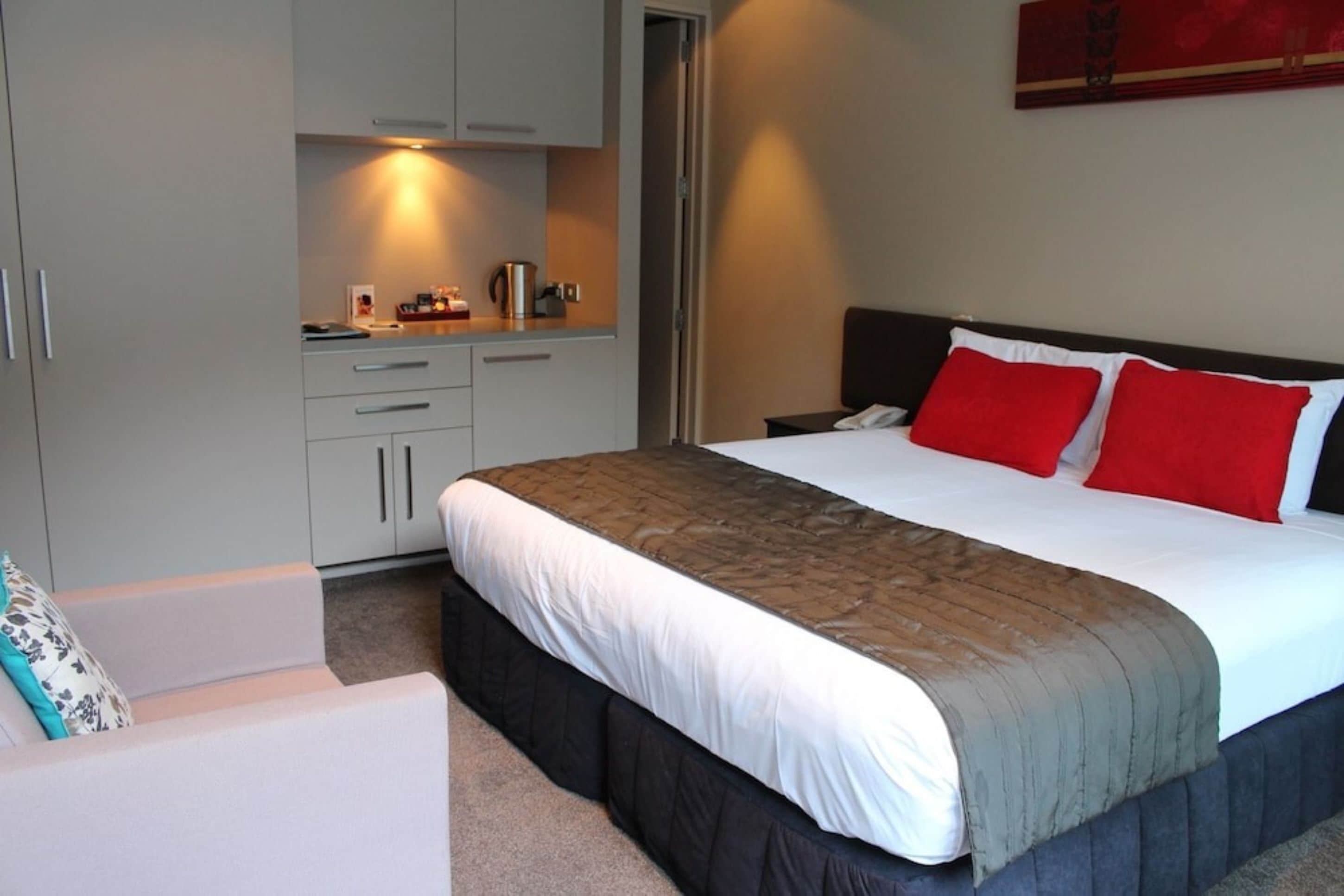 A hotel room with a bed, a bedside table, a desk with a chair, and a wardrobe.