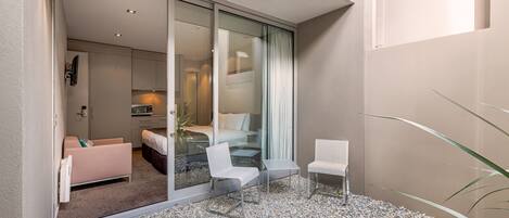 A modern hotel room with a sliding glass door leading to a balcony with a gravel floor, a bed, a sofa, and two chairs.
