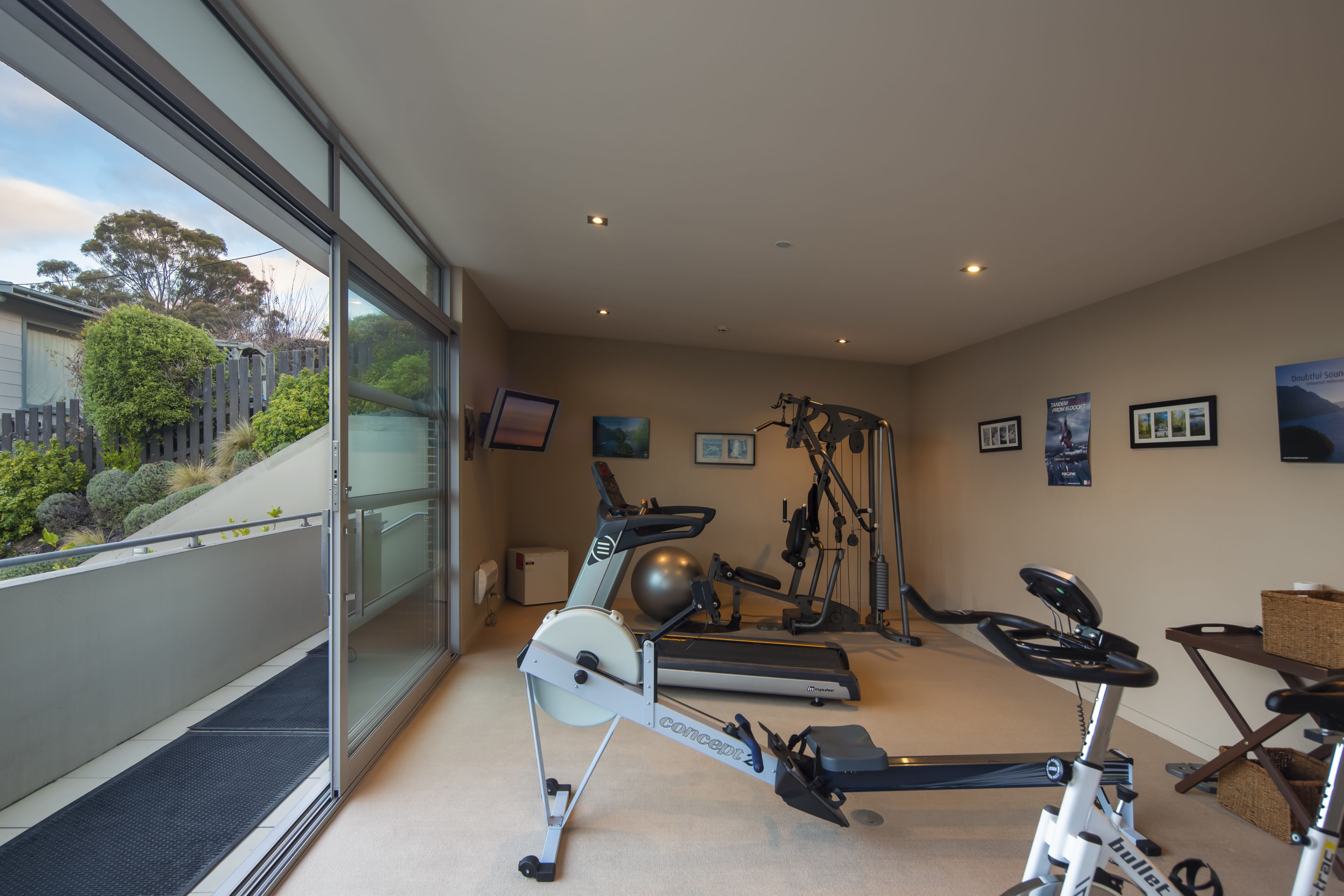 Une salle de sport à domicile équipée de matériel d’exercice, d’un tapis de course, d’un vélo d’appartement et d’un rameur.