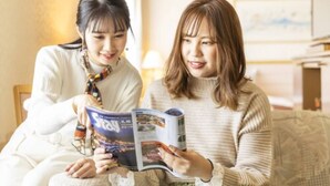 Dos personas sentadas en un sofá, leyendo una revista.