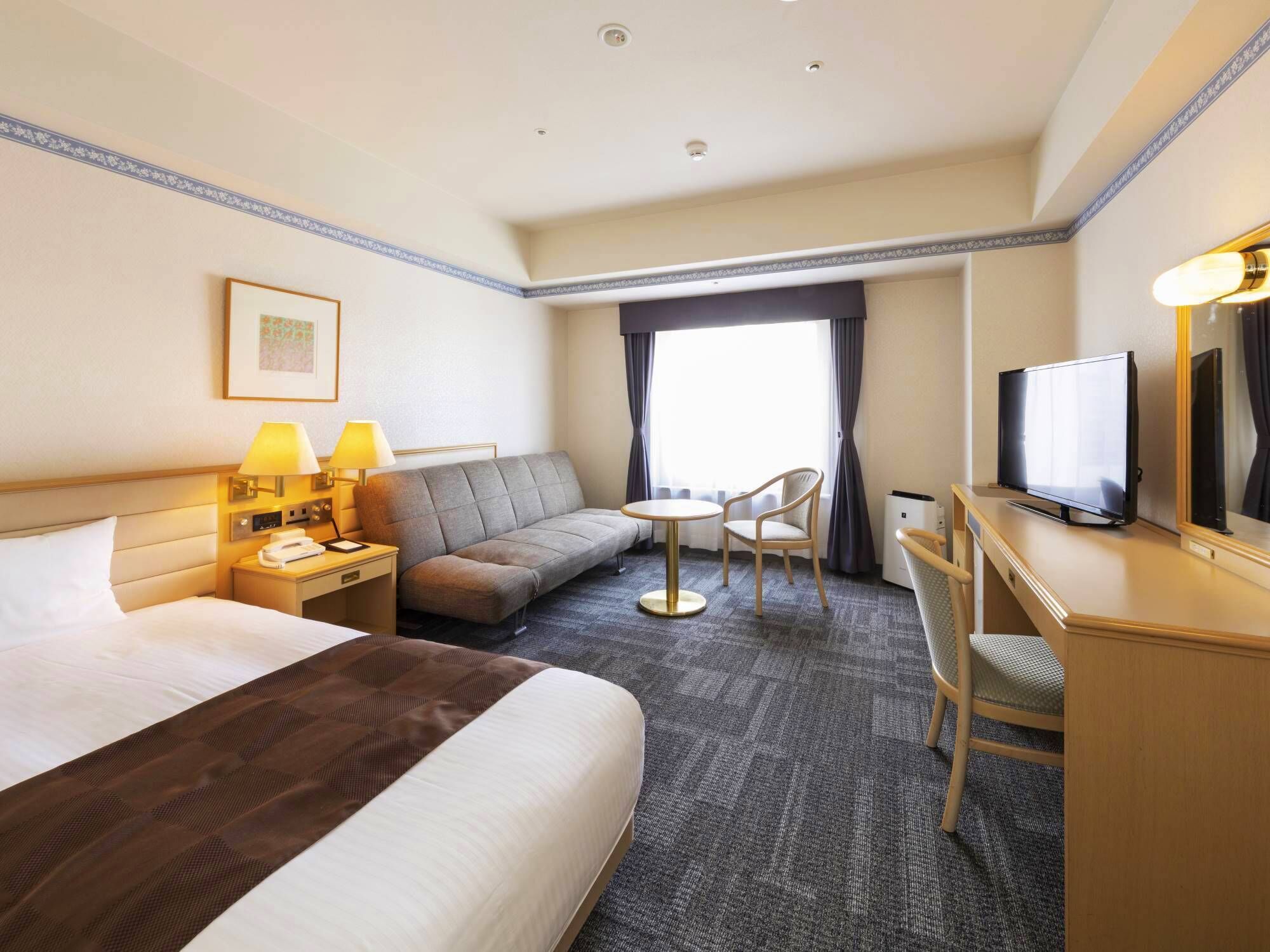 Habitación de hotel con cama, sofá, escritorio con televisor y silla.