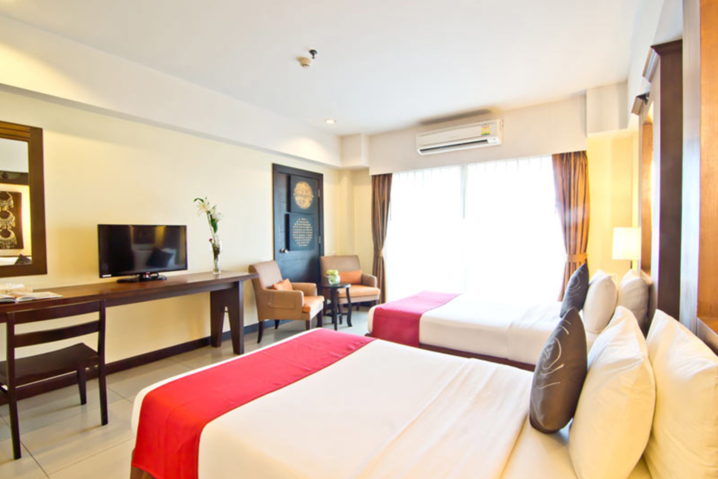 Une chambre d’hôtel avec deux lits, un bureau, une chaise, une télévision et un appareil de climatisation.