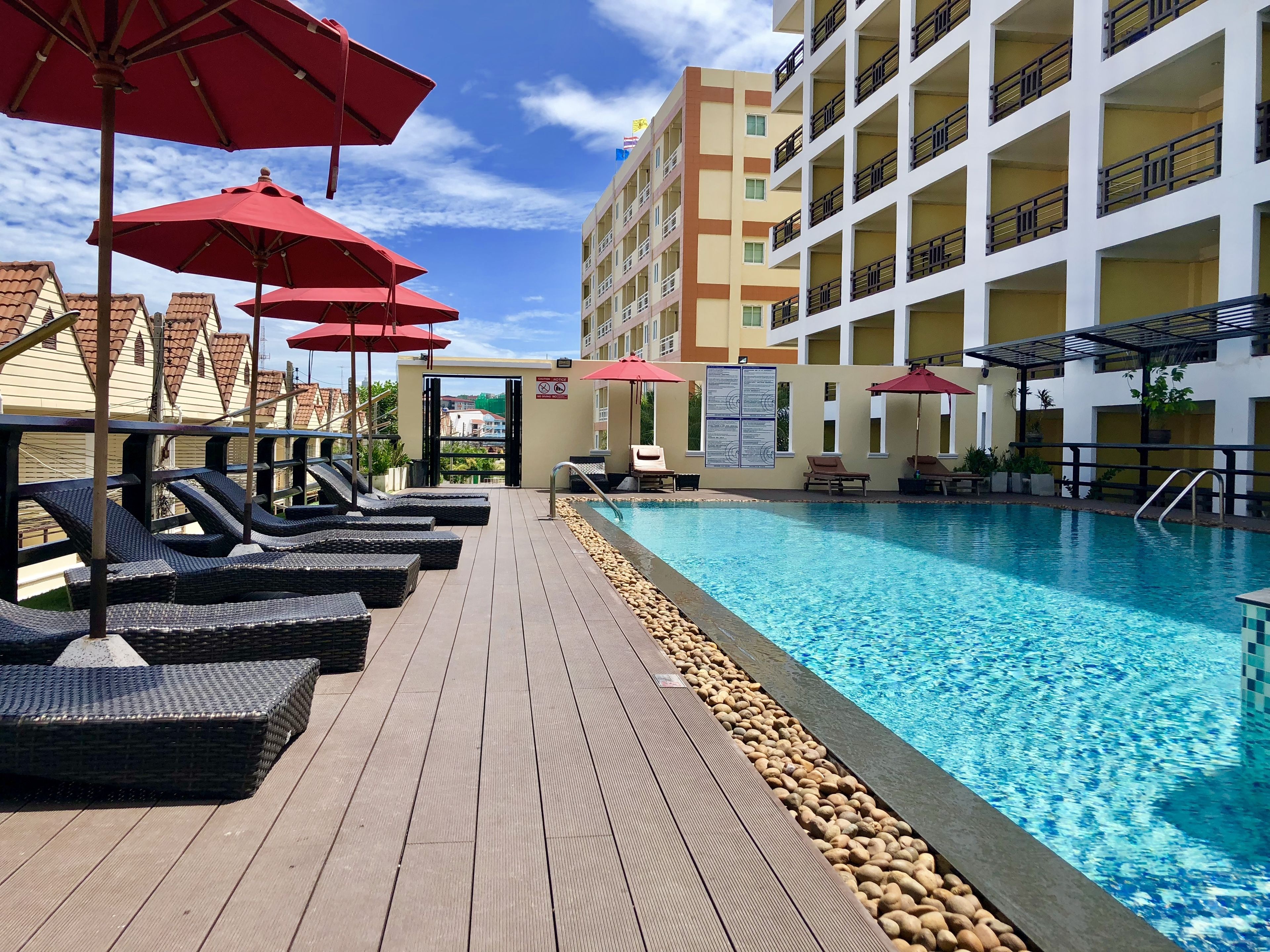 A poolside area with lounge chairs and umbrellas, a clear blue pool, and a building with balconies.