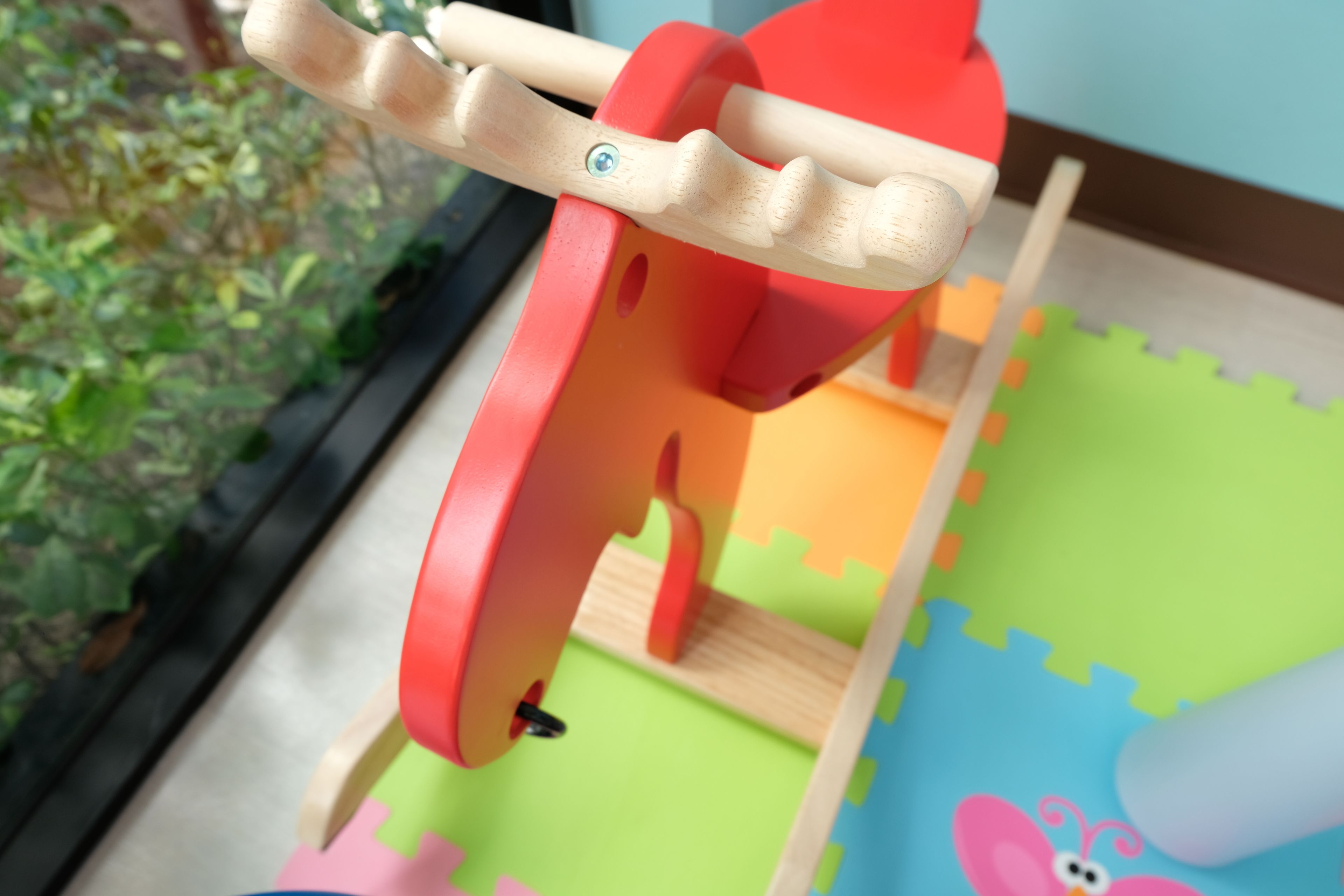 Ein Holzspielzeug mit rotem und beigem Griff, platziert auf einer bunten Spieledecke mit einer rosa Figur.
