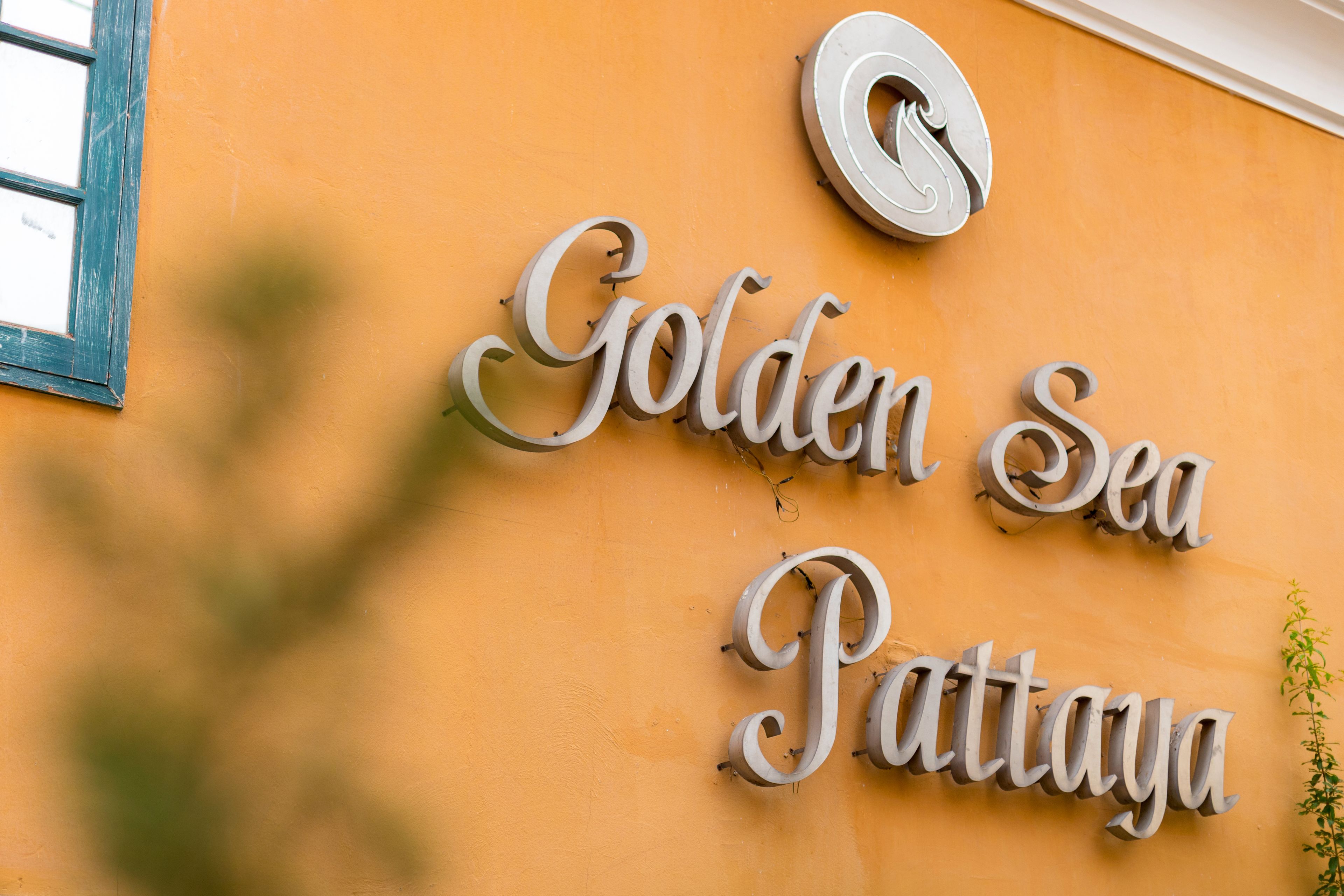 Et skilt med teksten "Golden Sea Pattaya" på en gul væg.