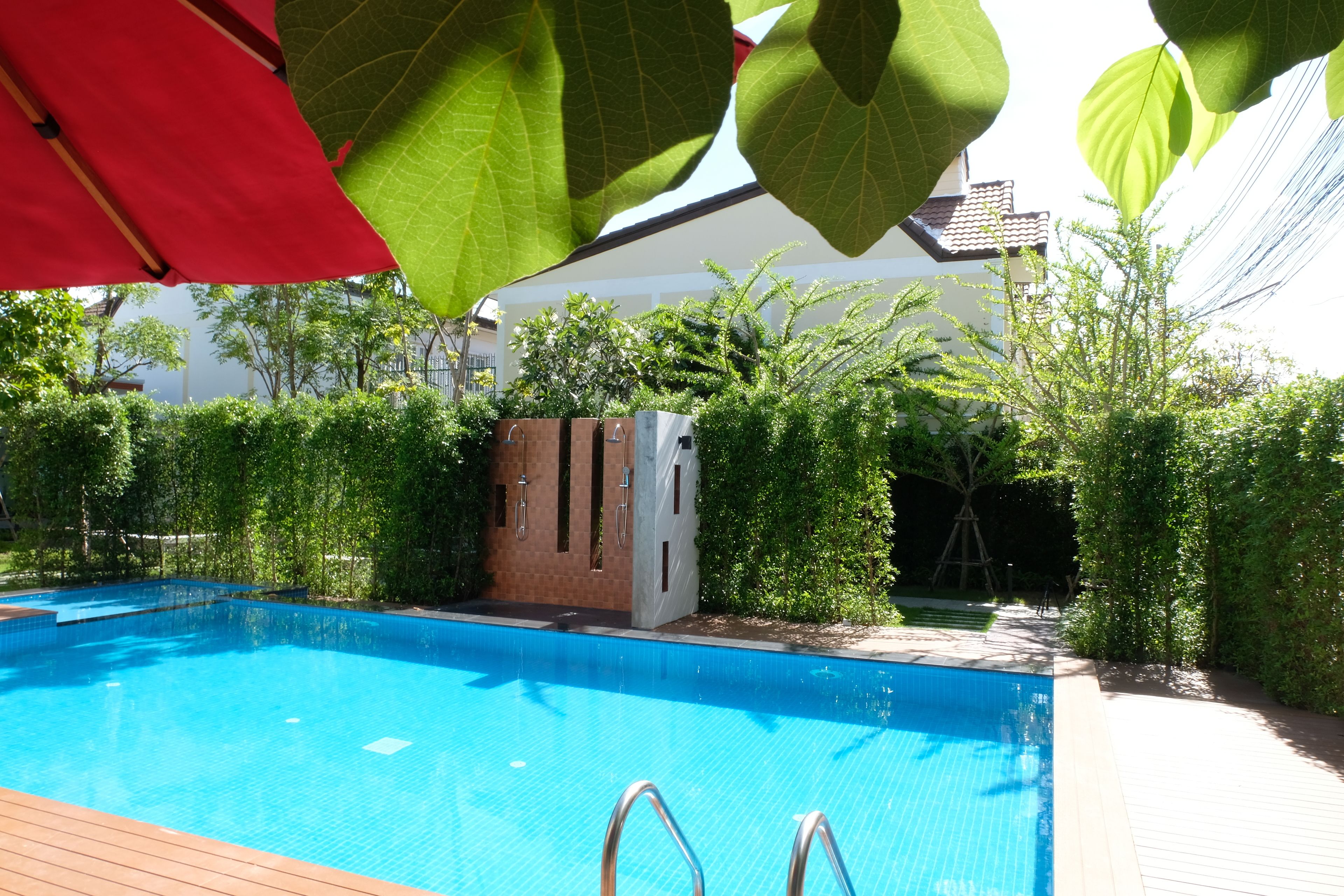 A swimming pool with a wooden deck, surrounded by greenery and a building in the background.