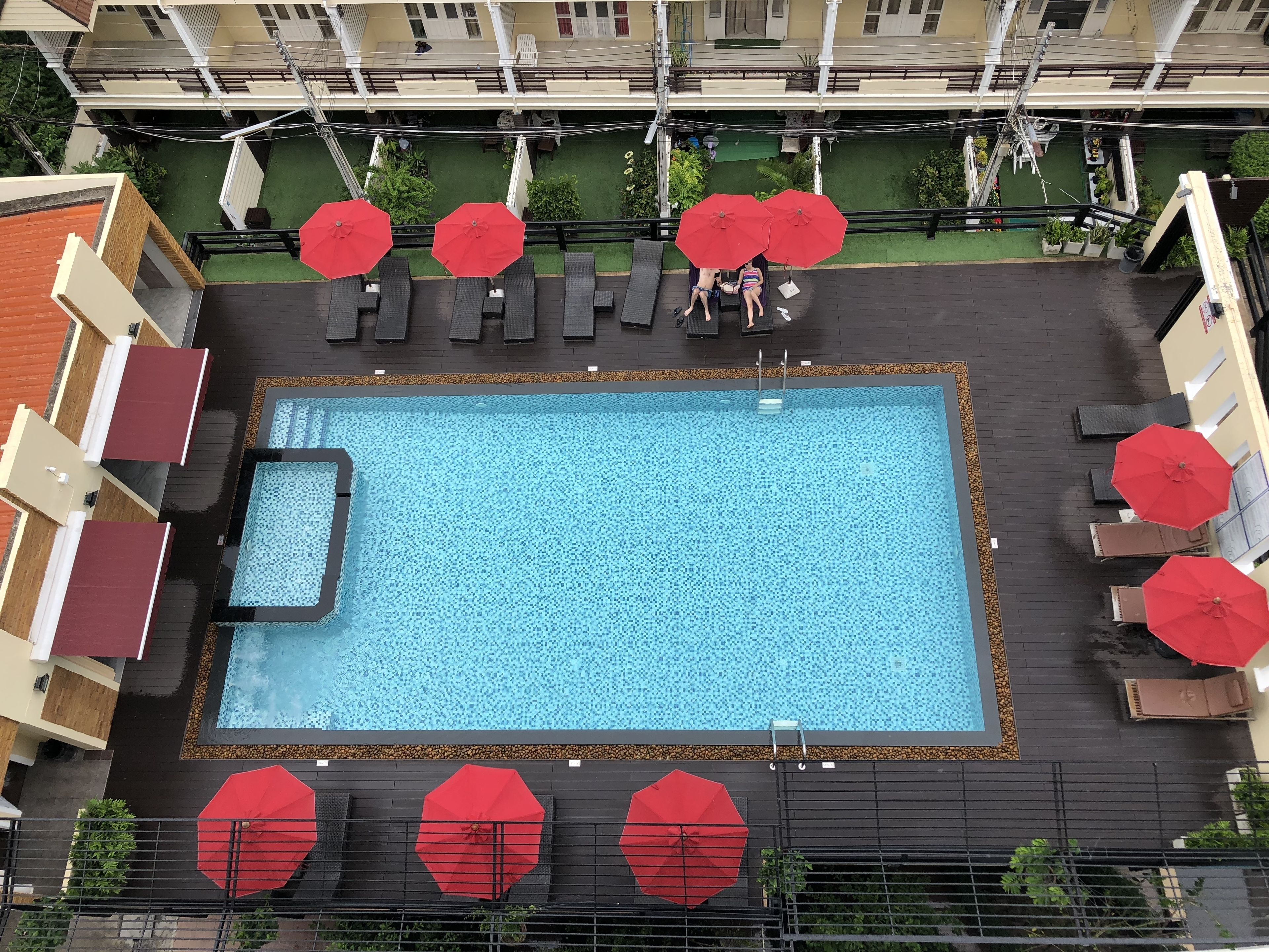 Vista aérea de una piscina en la azotea con varios sombrillas rojas, sillas de descanso y una pequeña zona de piscina.