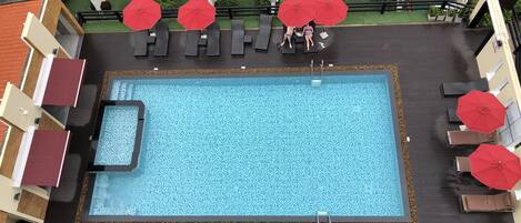 Vista aérea de una piscina en la azotea con varios sombrillas rojas, sillas de descanso y una pequeña zona de piscina.