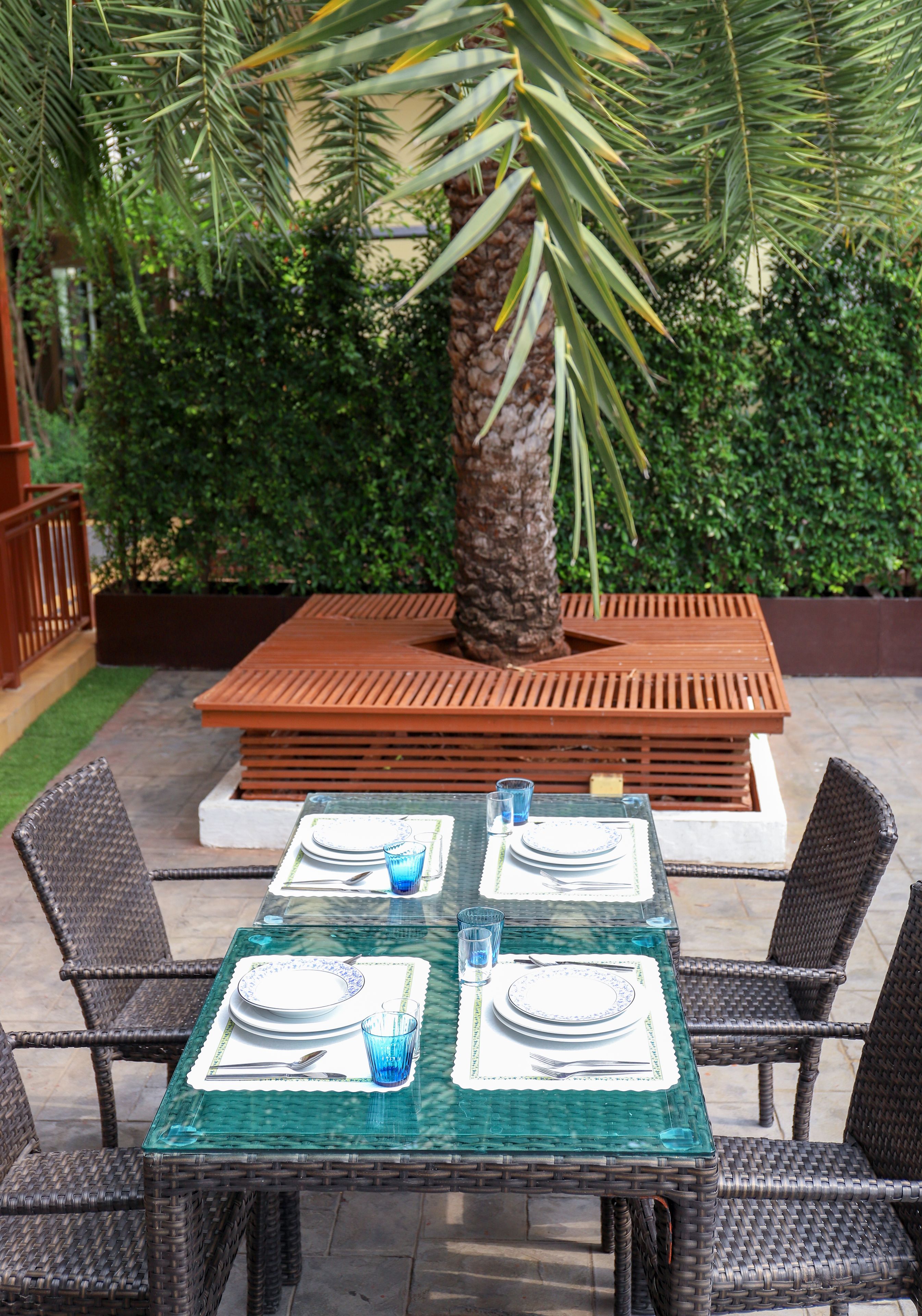 Een terras met eethoek, een tafel voor vier personen, omringd door rieten stoelen, en een houten bankje op de achtergrond.
