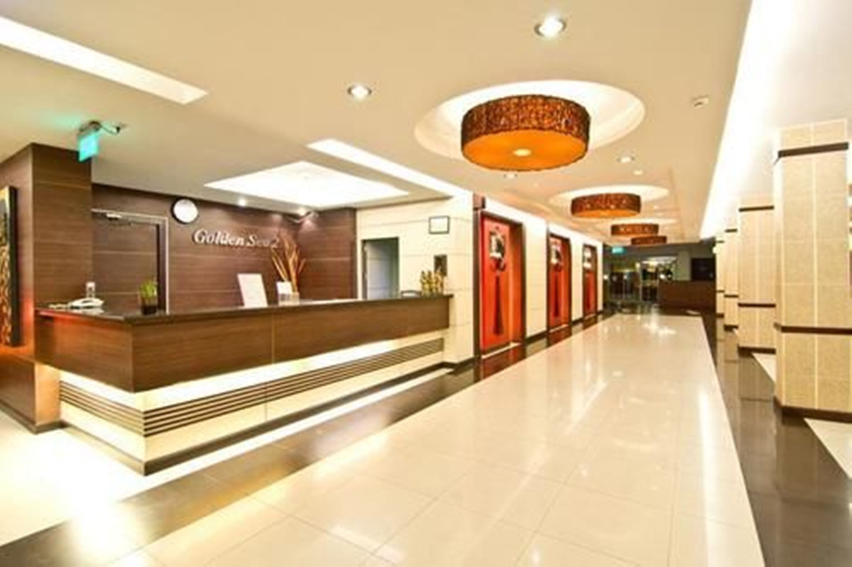 A hotel reception area with a modern design, featuring a reception desk, a sign that reads "Golden Suite," and a hallway with doors and a tiled floor.