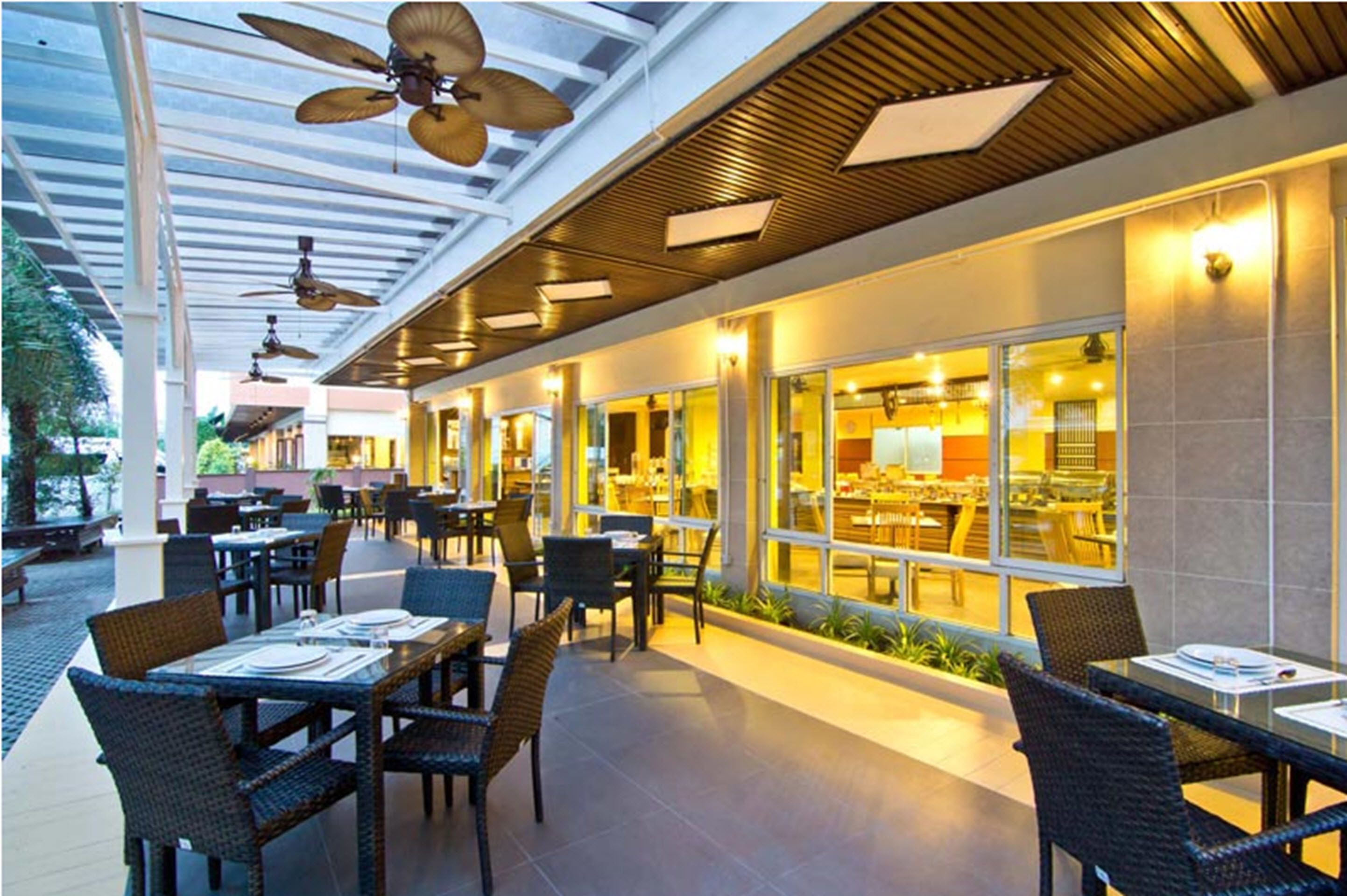 An outdoor dining area with tables and chairs, ceiling fans, and a view of the restaurant inside.