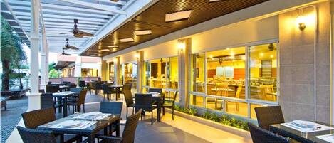 An outdoor dining area with tables and chairs, ceiling fans, and a view of the restaurant inside.