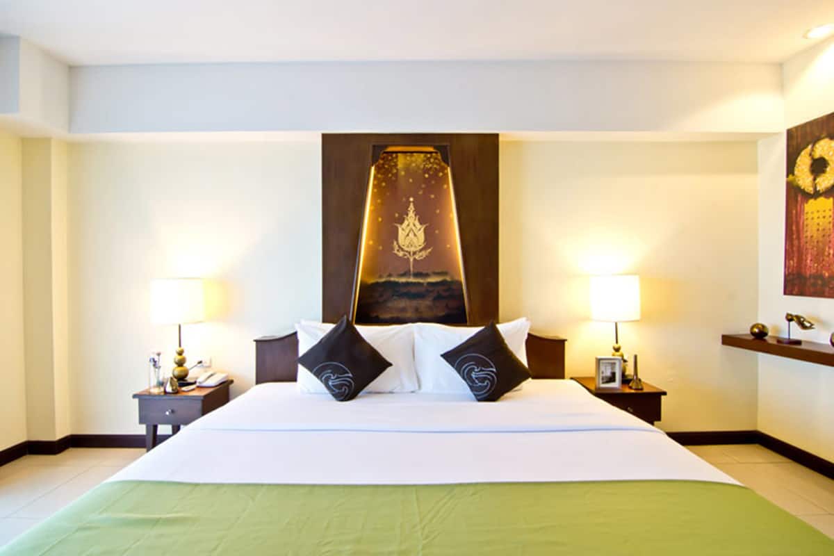 A hotel room with a large bed, two bedside tables, a nightstand, a wall-mounted artwork, and a framed picture on the nightstand.