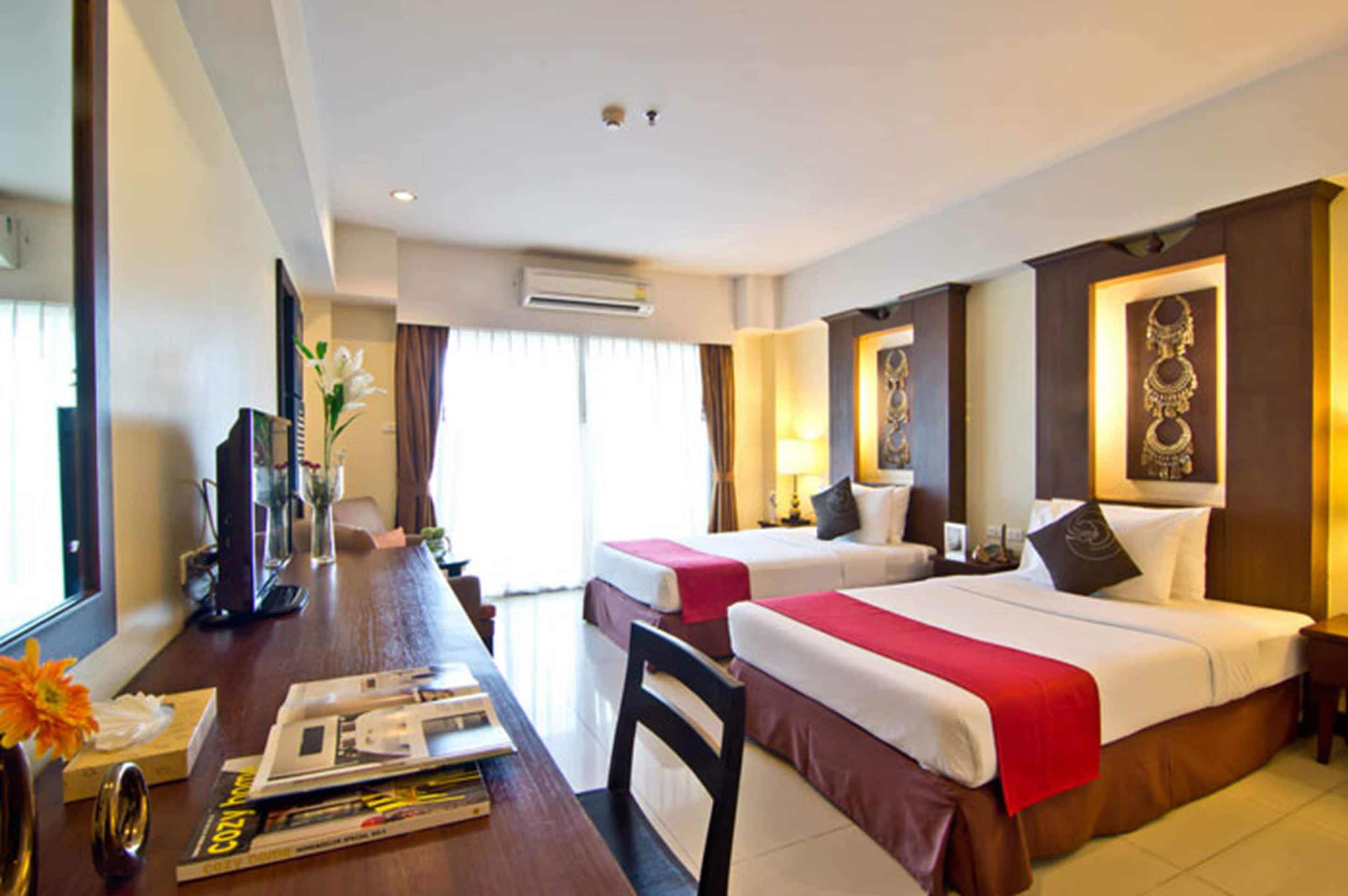 A hotel room with two beds, a desk with a computer, a chair, and a window with curtains.