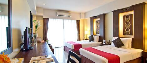 A hotel room with two beds, a desk with a computer, a chair, and a window with curtains.