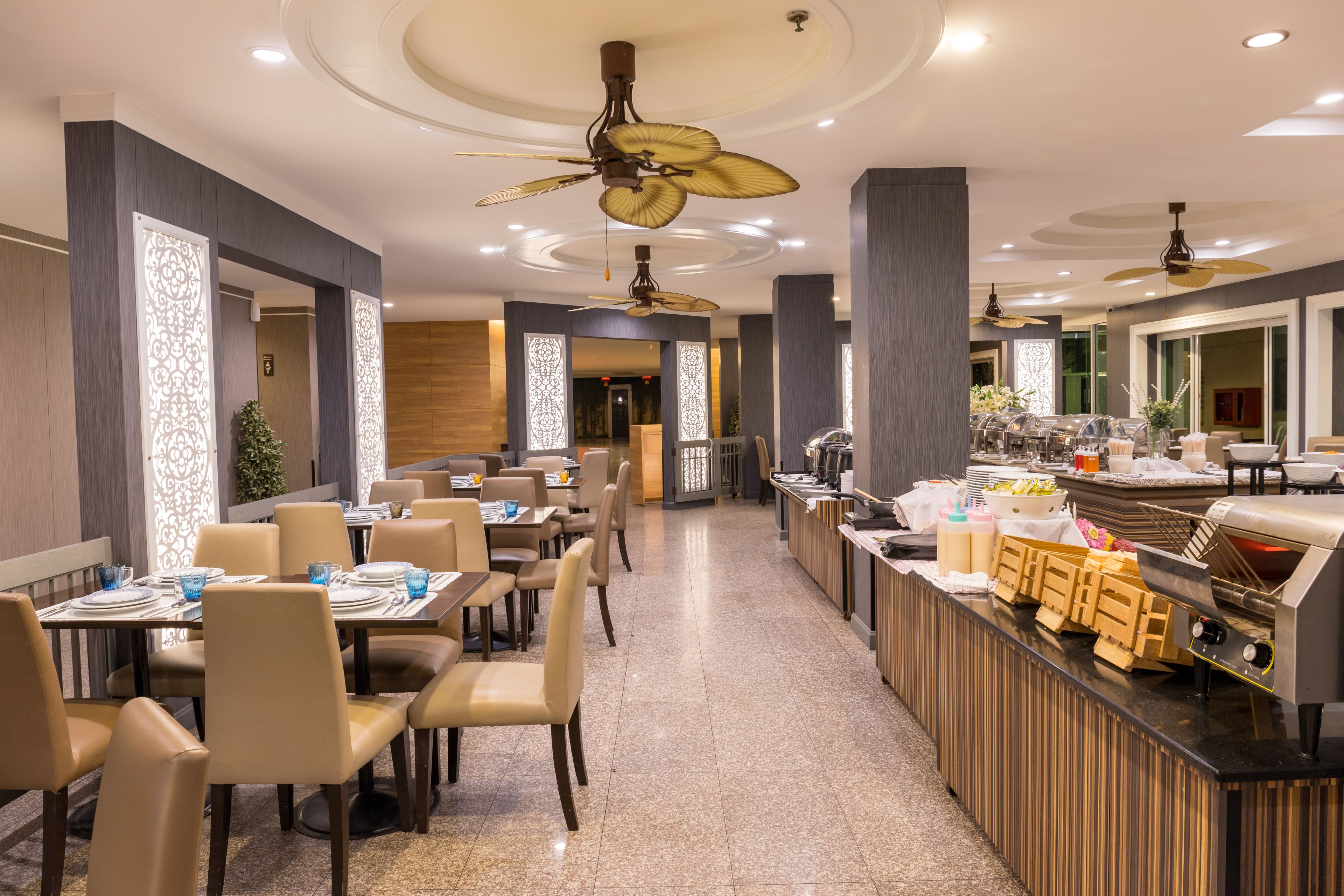 Un comedor moderno con varias mesas y sillas, ventiladores de techo y un mostrador tipo buffet.