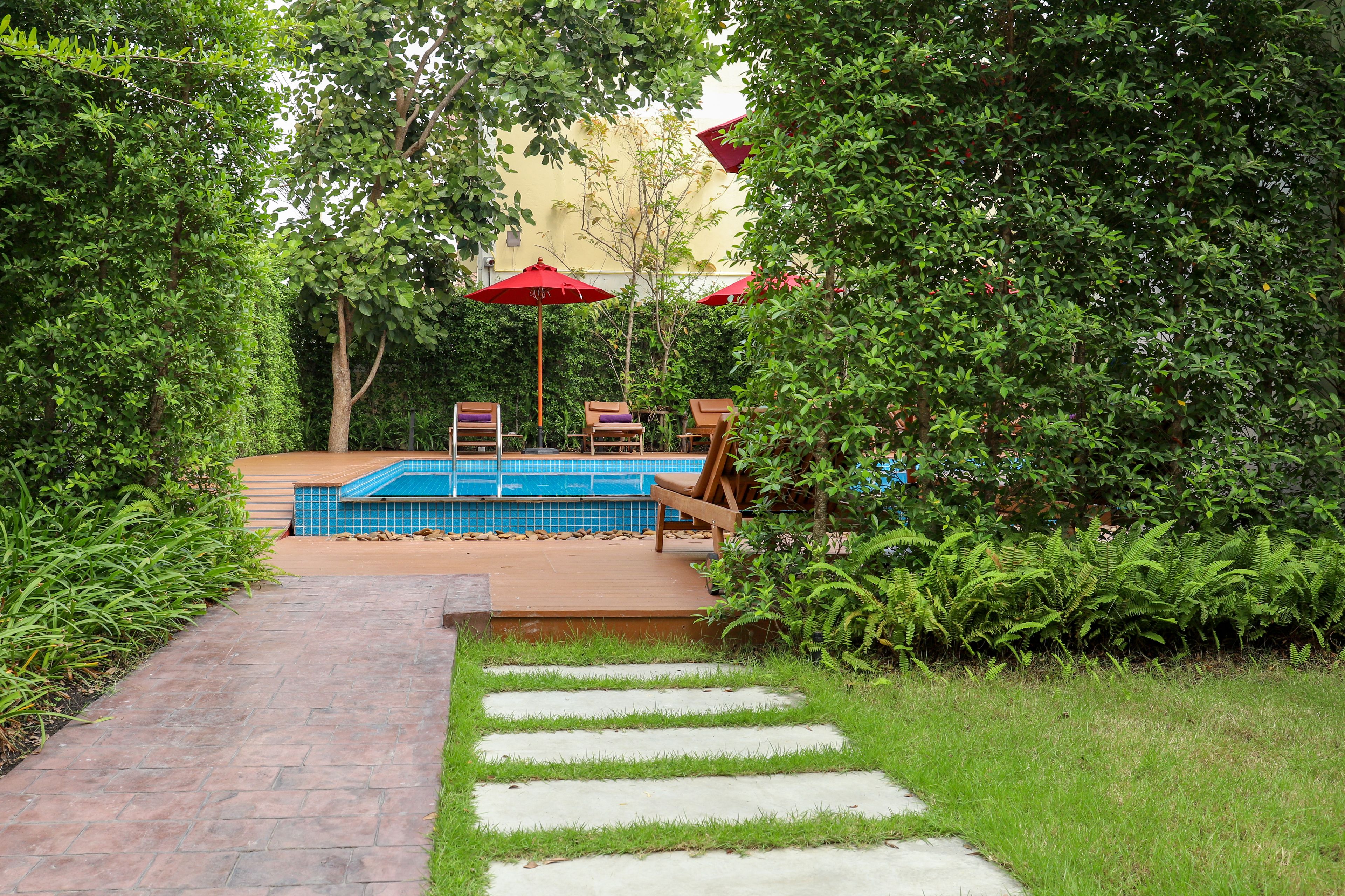 A pool area with a tiled deck, surrounded by lush greenery and red umbrellas.
