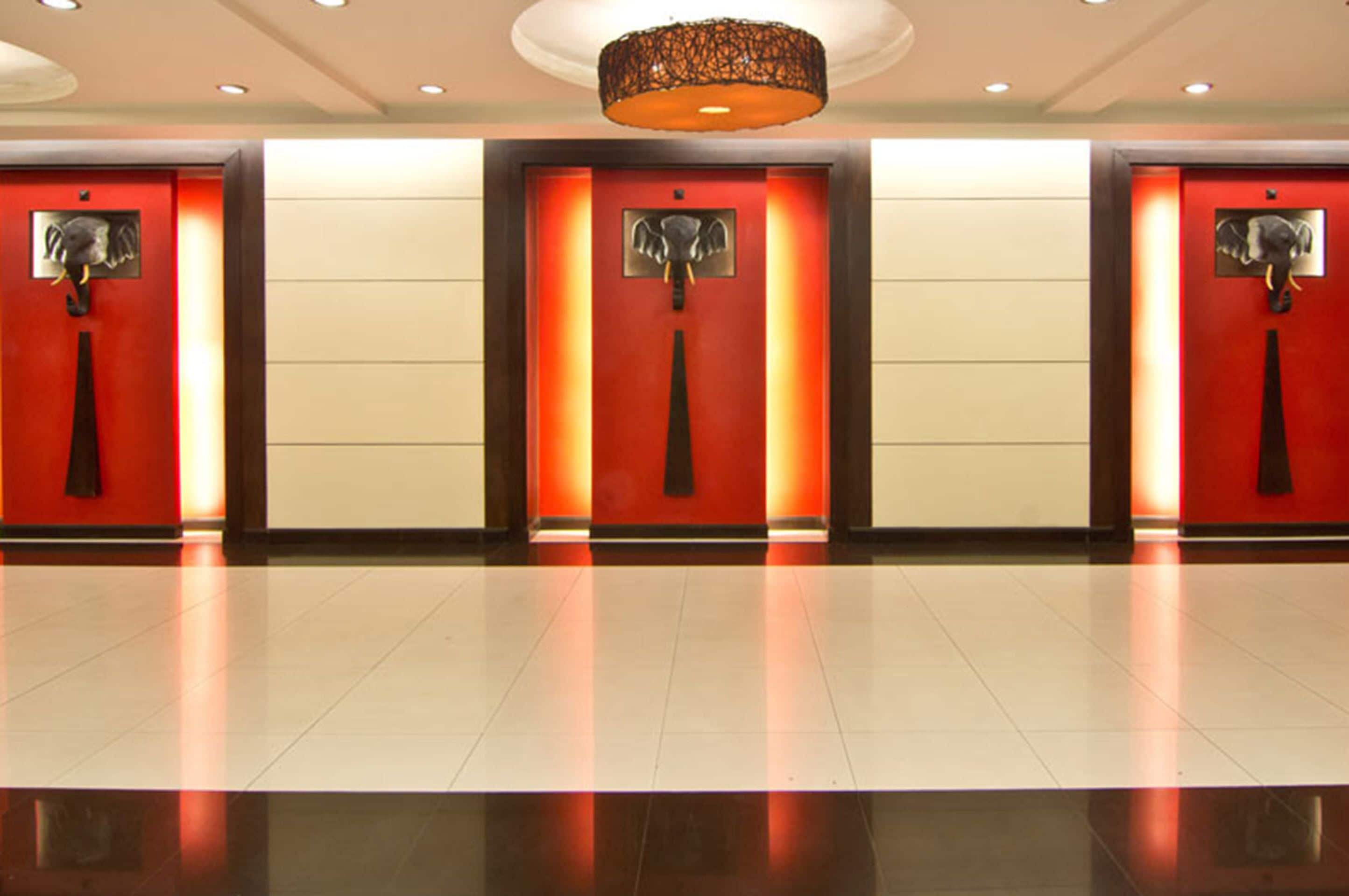 A hotel lobby with three elevator doors, each with a red panel and an elephant statue.